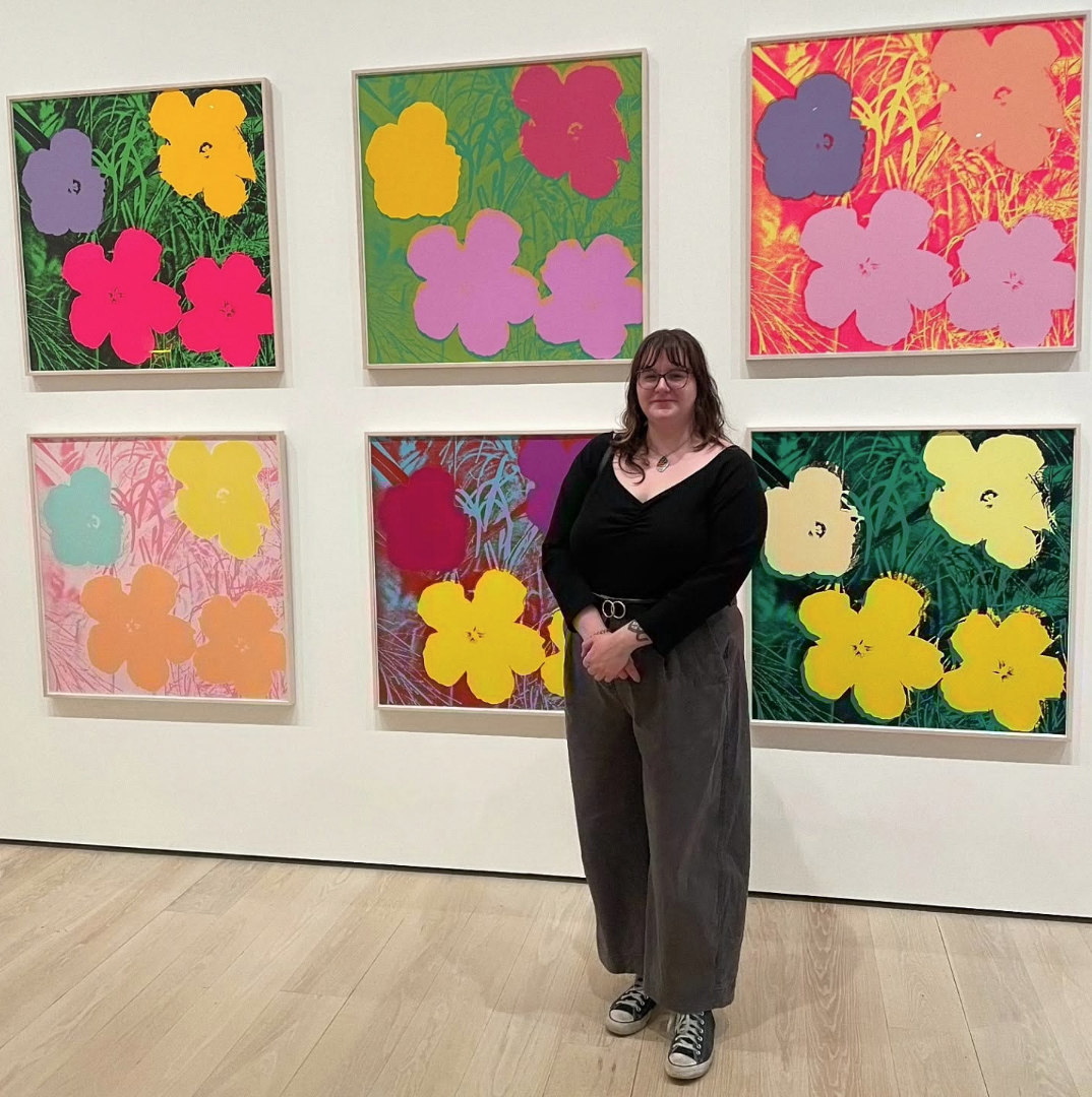 A young person standing in front of Andy Warhol flower paintings.